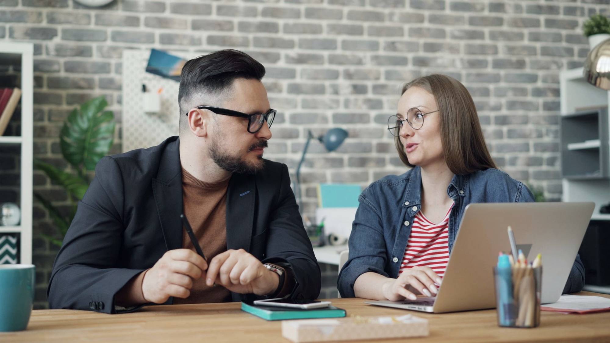 Two colleagues talking over a laptop in an office